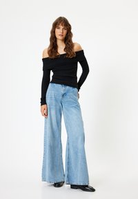 Top nero a coste senza spalline abbinato a jeans a gamba larga blu chiaro, caratterizzati da una vestibilità rilassata e scarpe scure in contrasto.