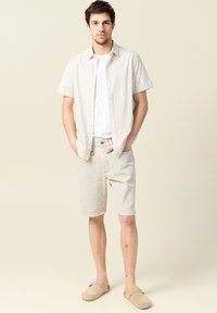Korte mouwen patroon blouse, lichtbeige shorts en beige instapper schoenen. Casual outfit met een ontspannen pasvorm en neutrale kleuren.