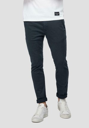 Chinos navy de algodón, diseño slim-fit, con puños enrollados y bolsillos laterales, combinados con zapatillas blancas.