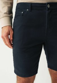 Sötétkék pamut rövidnadrág egyenes szabással, elülső zsebekkel és cipzáros, gombos zárással. Az anyag sima tapintású.