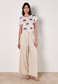 Top blanco de manga corta con estampado de elefante, combinado con pantalones beige de pierna ancha. Tejido ligero, corte relajado y detalle de cintura elástica.
