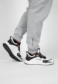 Zwart-witte sport schoenen met rode accenten. Heeft een textuur bovenwerk, een gevoerde kraag en contrasterende zolen voor grip.