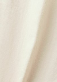 Tissu couleur crème avec une texture tissée subtile et des plis doux créant des ombres délicates.