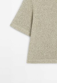 Harmaa neulottu lyhythihainen toppi, jossa on teksturoitu, rento istuvuus. Kangas on pilkullinen ja siinä on pyöreä pääntie.