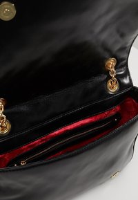 Svart läderhandväska med en glansig finish, guldiga detaljer, röd mönstrad tygfoder och ett zippat fack.