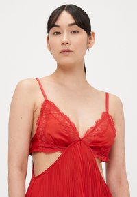 Punainen satiinirintaliivit pitsireunuksella, joissa säädettävät olkaimet ja laskostettu muotoilu. Sivussa olevat leikkaukset ja pehmeä tekstuuri korostavat niiden designia.