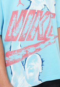 Gaiši zils īsām piedurknēm T-krekls izgatavots no kokvilnas, ar drosmīgu rozā "NIKE" grafiku un zilu silueta dizainu priekšpusē.
