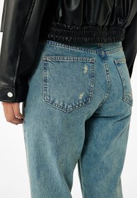 Vaqueros de mezclilla azul claro con un ajuste relajado, que presentan detalles deshilachados y bolsillos traseros. Combinados con una chaqueta de cuero negra elástica.