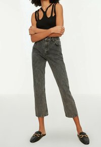 Top de tirantes negro de canalé con detalles recortados, pantalones vaqueros de mezclilla gris de talle alto y zapatos negros texturizados tipo slip-on con acentos dorados.