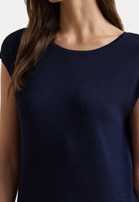 Námorně modrý top s krátkým rukávem vyrobený z žebrované látky, s lodičkovým výstřihem a hladkým povrchem, navržený pro pohodlné nošení.