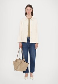 Beige cotton jacket, olive top, blue jeans, holding a tan suede bag, and wearing white pointed shoes. Simple and clean design with minimal details.