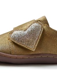 Zapato sintético dorado con un acabado texturizado, que presenta un prominente adorno brillante en forma de corazón y suela de goma marrón.