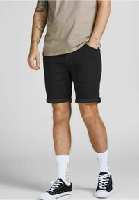 Czarne szorty dżinsowe z podwiniętymi brzegami, noszone z beżową koszulką, białymi skarpetkami i czarnymi sneakersami. Tkanina ma gładką teksturę.