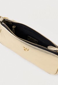 Χρυσή μεταλλική τσάντα χερούλι με χρυσό φερμουάρ, μικρό χρυσό λογότυπο και μαύρο ύφασμα εσωτερικά με εσωτερική τσέπη με φερμουάρ.