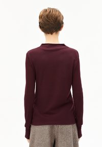 Bordeaux longsleeve top met een ronde hals, soepele textuur en aansluitend ontwerp. Draagt met grijs gestructureerde broeken, gezien van achteren.