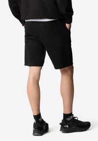 Pantalones cortos de algodón negros con un ajuste relajado, que cuentan con bolsillos y una textura suave, llevados con zapatillas deportivas negras y calcetines.