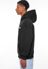Sort oversized hoodie med en kængurulomme, ribbede manchetter og kant. Har et hvidt logo på brystet. Blød stoftekstur.