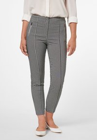 Pantalons à motif carreaux noir et blanc avec une coupe slim, dotés de poches latérales et d'une texture de tissu lisse. Portés avec des chaussures blanches.