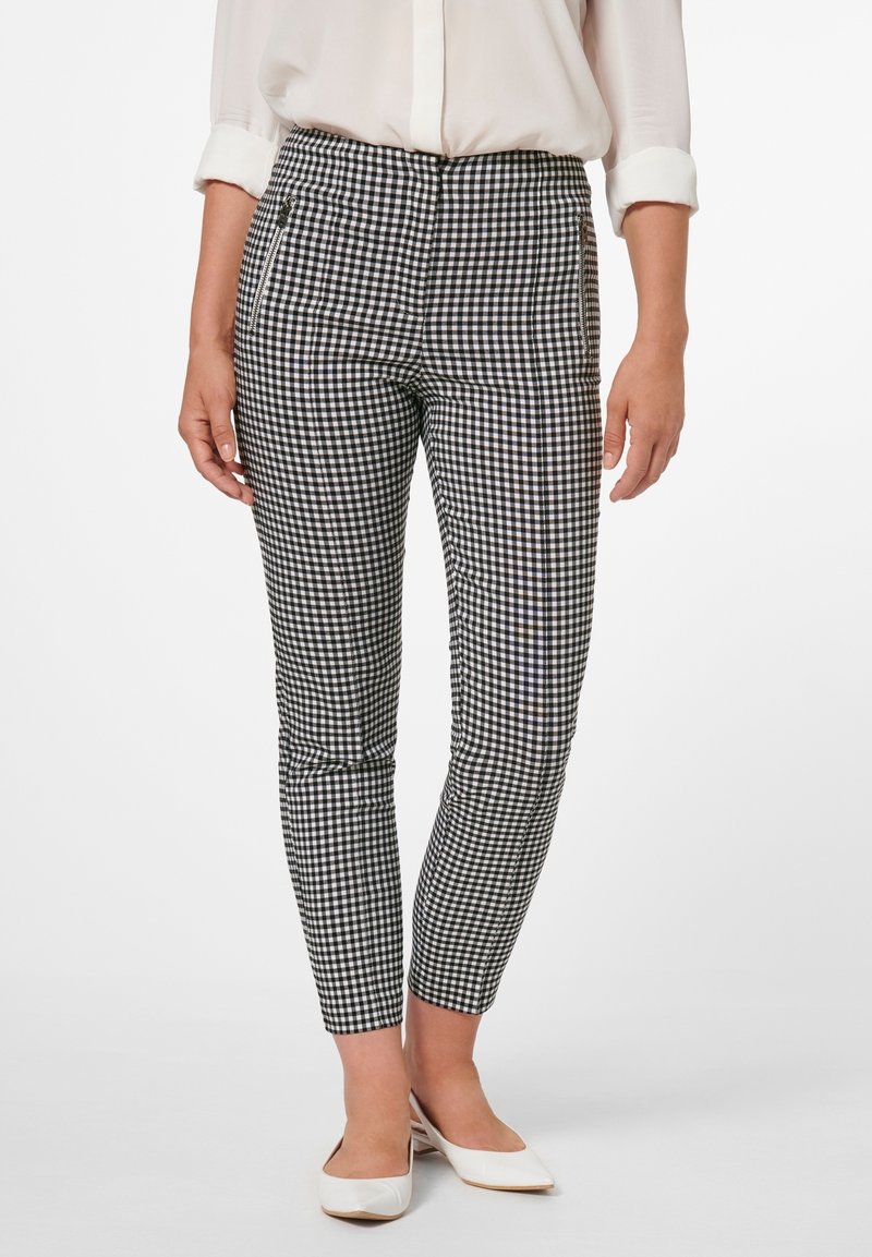 Pantalons à motif carreaux noir et blanc avec une coupe slim, dotés de poches latérales et d'une texture de tissu lisse. Portés avec des chaussures blanches.
