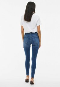 Jean skinny bleu taille haute avec un design ajusté, fabriqué en denim. Comprend deux poches arrière et est associé à un t-shirt blanc uni.