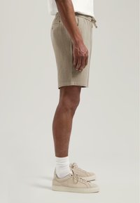 Beige teksturerte shorts med strikk i livet, sidelommer og en avslappet passform, kombinert med nøytrale joggesko og hvite sokker.