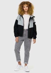 Color-blocked jacket in black and light gray with zip closure, elastic cuffs, and drawstring hood. Paired with gray jeans and white sneakers.