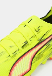 Helekollane jalgpalliklots tekstuurse pealiskihiga, millel on mustad ja punased detailid, kuus paela ja ümarad naelad haarduvuse tagamiseks.