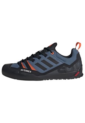 Black and gray climbing shoes featuring a mesh upper with orange accents, a reinforced toe cap, and a textured rubber sole for grip.