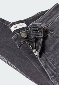 Jean en denim gris foncé avec fermeture éclair ouverte, bouton fermé et étiquette de marque MNG visible à l’intérieur de la ceinture, indiquant la taille.