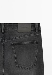 Jeans in denim nero con tasca posteriore, dettagli cuciti e un'etichetta rettangolare con il logo "Massimo Dutti" in rilievo.