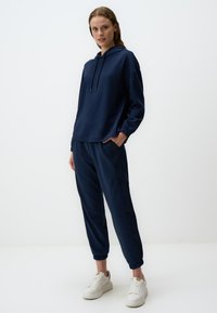 Felpa blu navy con cappuccio e coulisse, vestibilità rilassata e polsini elasticizzati, abbinata a pantaloni jogger coordinati con tasche laterali e caviglie a coste.