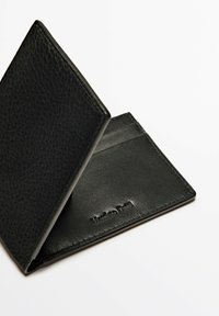 Portafoglio in pelle nera con una superficie testurizzata, due slot per carte all'interno e logo del marchio impresso. Si apre per rivelare una fodera interna liscia.
