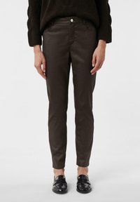 Brązowe, slim-fit spodnie o gładkim wykończeniu i przednich kieszeniach, w połączeniu z czarnymi lakierowanymi loafersami. Minimalistyczny design.