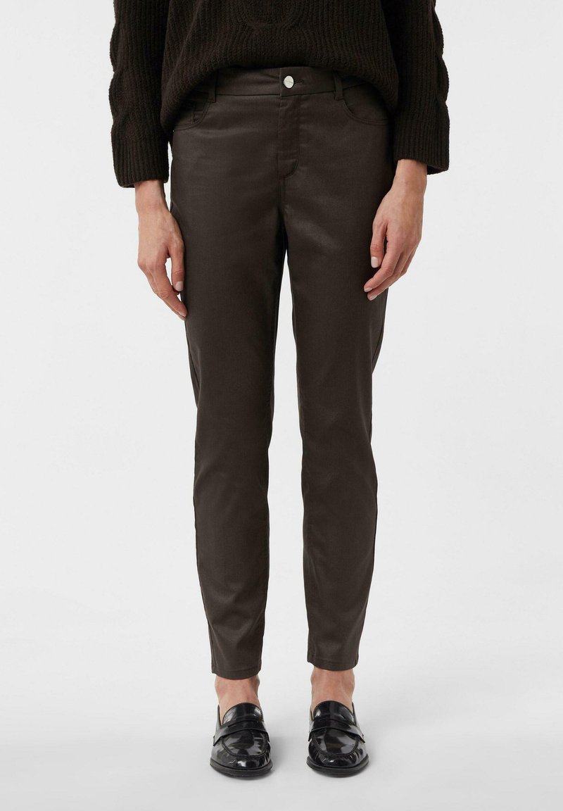 Brązowe, slim-fit spodnie o gładkim wykończeniu i przednich kieszeniach, w połączeniu z czarnymi lakierowanymi loafersami. Minimalistyczny design.