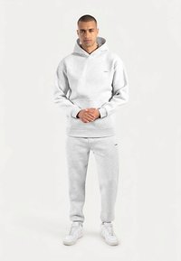 Grauer Baumwoll-Hoodie mit Kängurutasche und passender Sweatpants. Mit entspanntem Schnitt und gerippten Bündchen. Weiße Sneakers runden den Look ab.