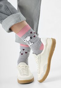 Graue Socken mit pinken Bündchen, verziert mit einem Cartoon-Hund und Herzen. Getragen mit weißen Sneakern und hochgekrempelten grauen Jeans.