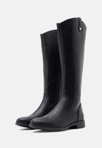 Botas de cuero negro hasta la rodilla con punta redonda, textura suave, cremallera lateral y diseño minimalista. Presenta un tacón bajo y rectangular.