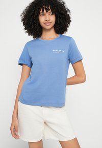 Kék pamut rövid ujjú póló, kerek nyakkivágással és elöl "GANT1949" felirattal. Fehér sorttal párosítva. Sima textúrájú, laza kialakítású.