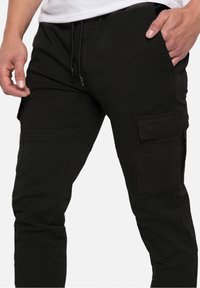 Pantalon cargo noir avec une coupe slim, une taille élastique avec cordon de serrage, et plusieurs poches latérales pour plus de fonctionnalité.