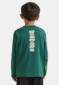 Maglietta a maniche lunghe verde con scollo rotondo e logo verticale bianco "DIADORA" sulla schiena. Tessuto in cotone liscio, vestibilità casual.