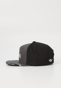 Μαύρο και γκρι καπέλο snapback με επίπεδη γείσο, που διαθέτει κεντημ�ένο λογότυπο μπροστά και λευκή λεπτομέρεια στο πλάι.