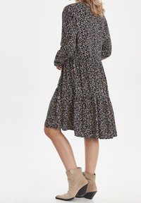 Blommönstrad klänning med långa ärmar, lager-på-lager kjol och rund halsringning. Svart bakgrund med flerfärgade blommor. Matchad med beige ankelstövlar.