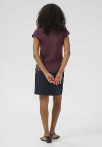 Haut bordeaux à manches courtes avec une coupe décontractée, associé à une jupe sombre arrivant au genou. Des chaussures marron foncé complètent la tenue.