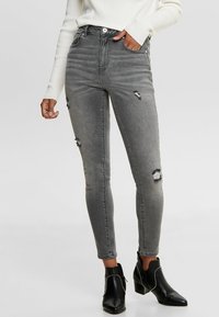 Jeans skinny de tiro alto en gris con detalles desgastados, ajuste slim, cinco bolsillos y un ligero desvanecimiento, combinados con botas negras de tobillo.