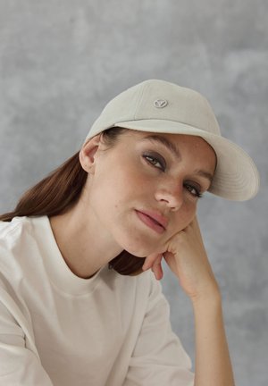 Hellgraue Baseballmütze mit runder Krone, flachem Schild und gesticktem Logo auf der Vorderseite. Das Model trägt einen cremefarbenen Sweatshirt.
