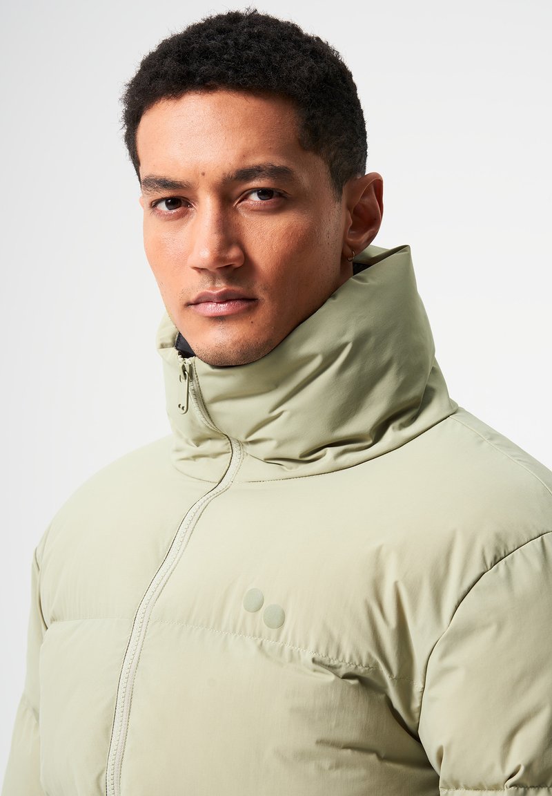 Hellgrüne Steppjacke mit hohem Kragen und Reißverschluss, ausgestattet mit einer matten Oberfläche und zwei runden Akzenten auf der Brust.
