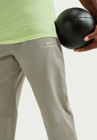 Αθλητικά ρούχα Nike Pro με ανοιχτοπράσινο πουκάμισο και γκρι παντελόνια. Τα παντελόνια είναι λείες, με διατρήσεις και λογότυπο Nike σε ανοιχτοπράσινο. Κρατιέται μαύρη μπάλα.