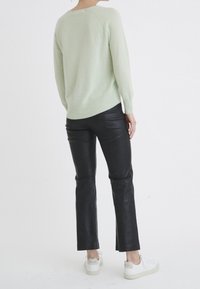 Pull en tricot vert clair, poignets et ourlet côtelés. Pantalon en cuir noir à jambe droite. Baskets blanches avec des accents texturés.