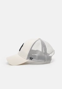 Beige Kappe mit einer soliden Front, Mesh-Rückseite und einem schwarzen Logo. Geformter Schirm und verstellbarer Riemen auf der Rückseite. Strukturierte Materialien und Nähdetails.