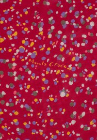 Tissu rouge présentant un motif moucheté multicolore avec des points violets, jaunes, roses et verts. Logo "Manila Grace" en or. Texture douce.